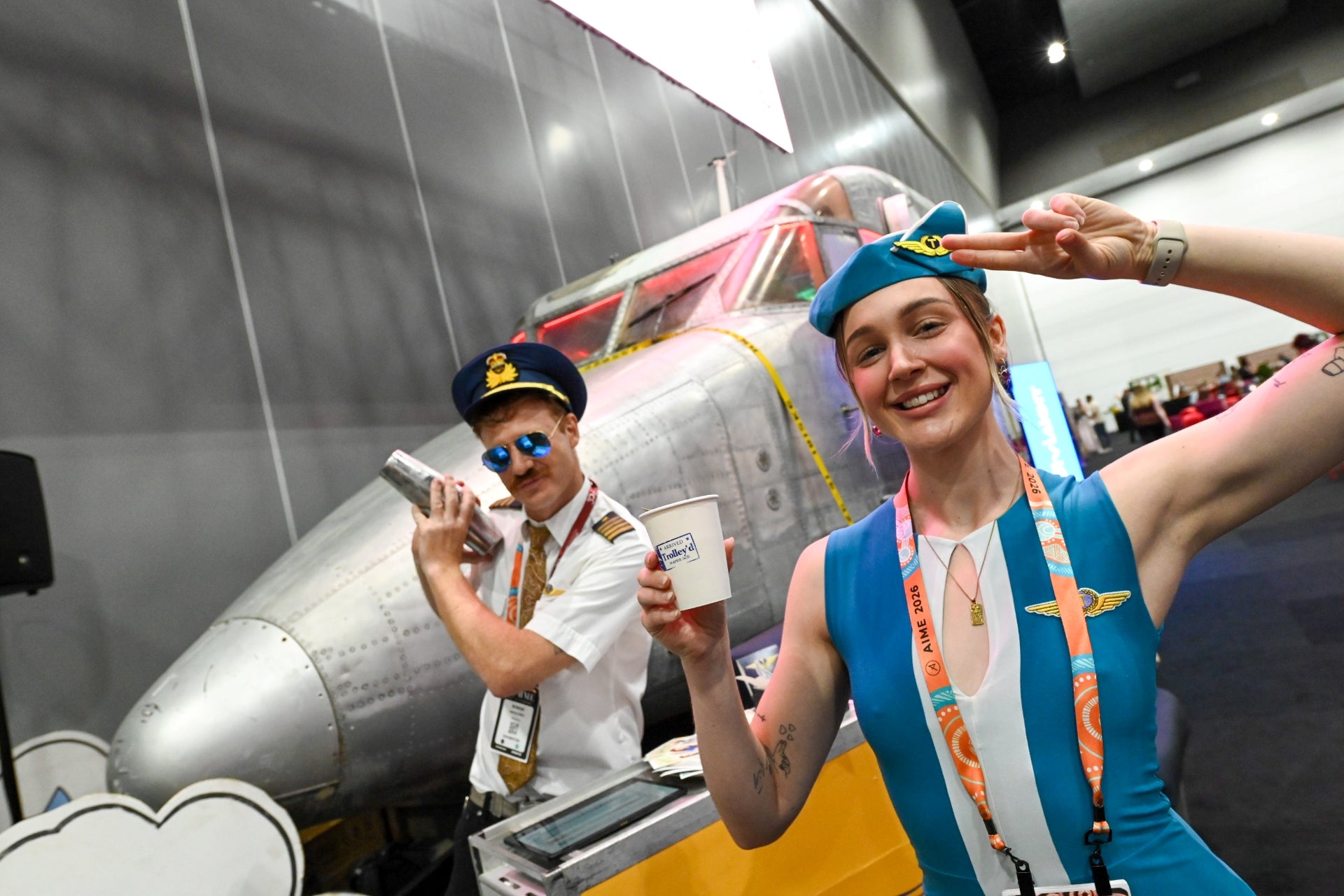 Trolley’d flight attendant serving cocktails in front of aircraft installation at AIME 2026 Hosted Buyer Lounge Melbourne