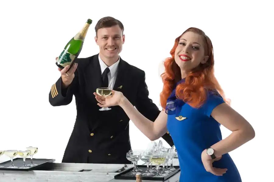 A green champagne bottle with a gold foil-wrapped cork and label, held by a man in a dark navy pilot’s uniform.