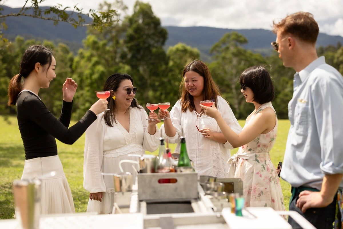 Guests toasting pink botanical cocktails beside airline trolleys in the Southern Highlands