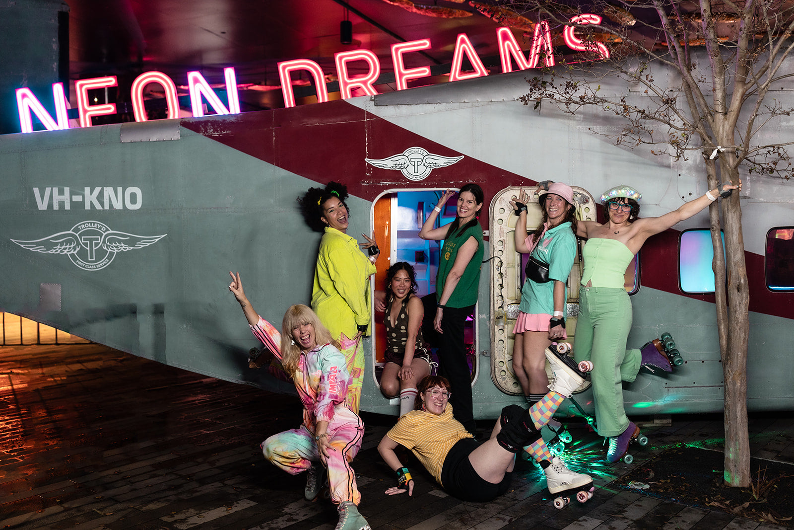 Guests and roller skaters posing outside the Neon Dreams aircraft installation at Vivid Sydney 2025