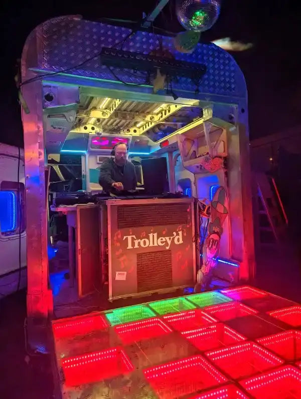 A retro-styled, metallic silver mobile dj booth with a ’trolley’d’ logo on its front panel and illuminated led dance floor below.