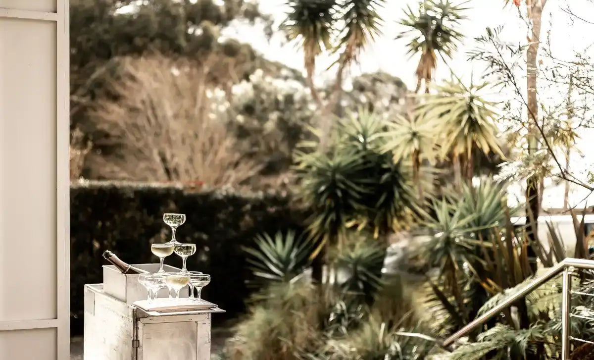 A set of clear, elegant champagne flutes arranged in a tiered display on a white serving cart.