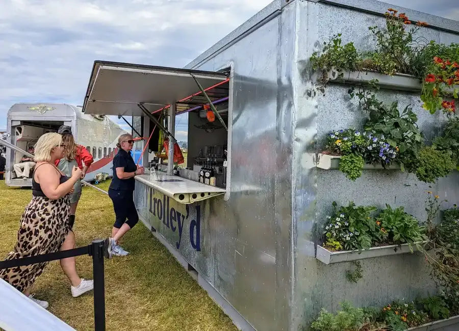 Silver metallic food truck with vertical garden panels and blue lettering.
