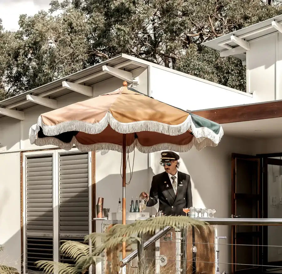 A stylish, multi-toned patio umbrella with a beige and green canopy edged in white fringe.