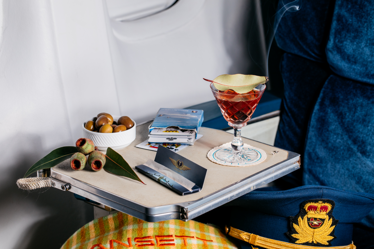 First class in-flight cocktail with eucalyptus garnish, olives and playing cards on vintage airline tray table – Trolley’d sustainable bar service