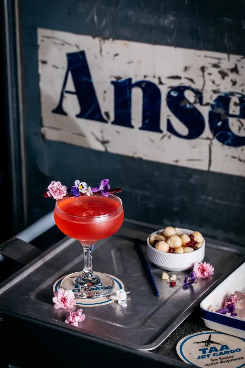 Cocktail with floral garnish on a tray with 'Ansett' sign in the background