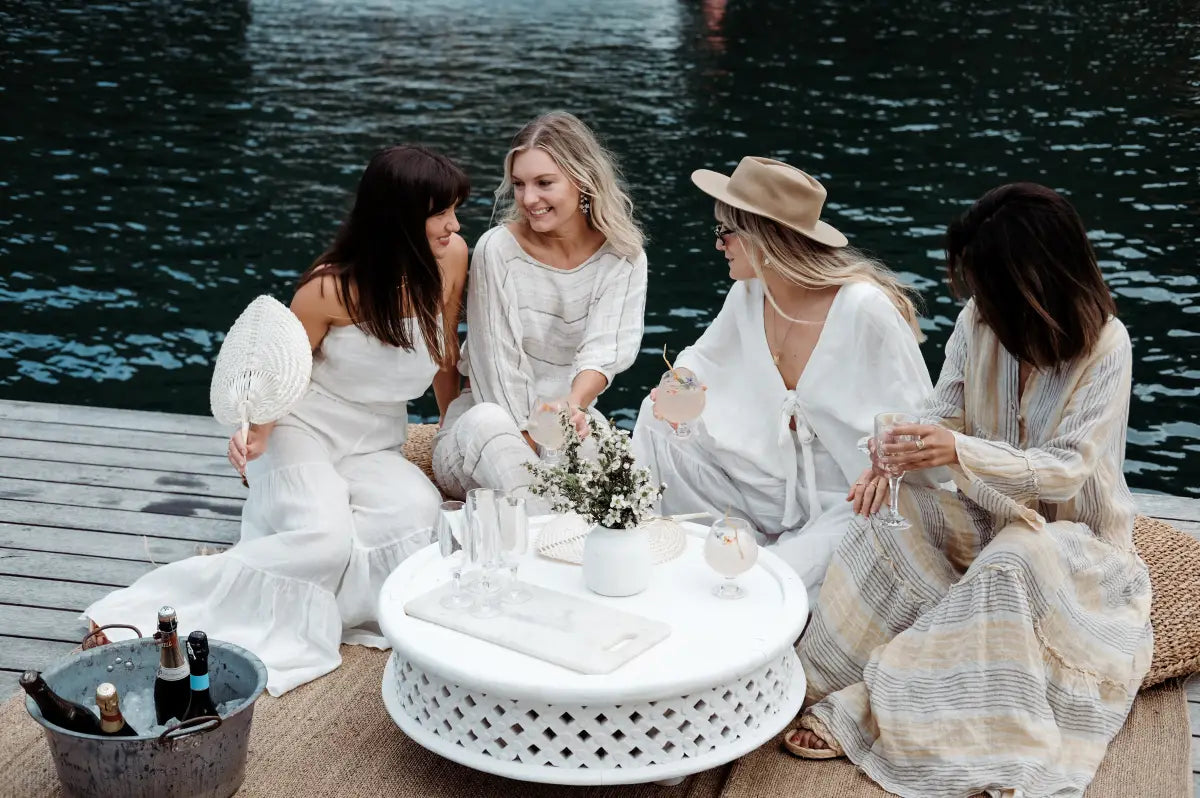 A group of friends in white outfits enjoying drinks and food at an elegant outdoor dining setup provided by Trolley’d.