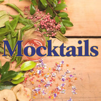 A promotional image for Trolley'd Mocktails featuring a glass of pink mocktail surrounded by fresh leaves, berries, and edible flowers on a wooden surface, with the word "Mocktails" prominently displayed.