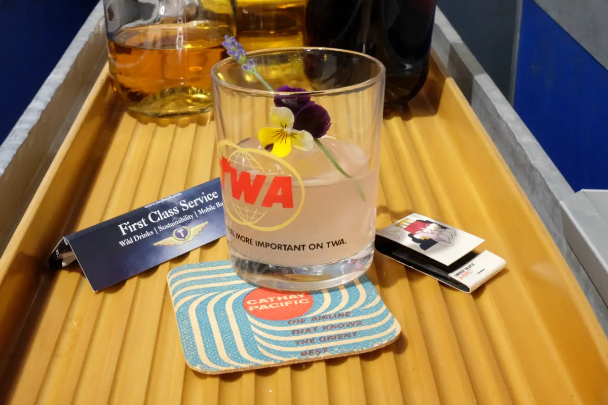 A glass of mulberry-infused clarified milk punch garnished with a flower, displayed with ingredients.