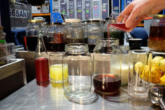 Hand pouring Illawarra plum syrup into a jar to prepare clarified milk punch.