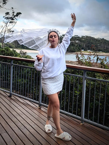 A bride-to-be in a veil raising her glass and celebrating outdoors with a scenic backdrop, holding a Trolley’d custom cocktail.