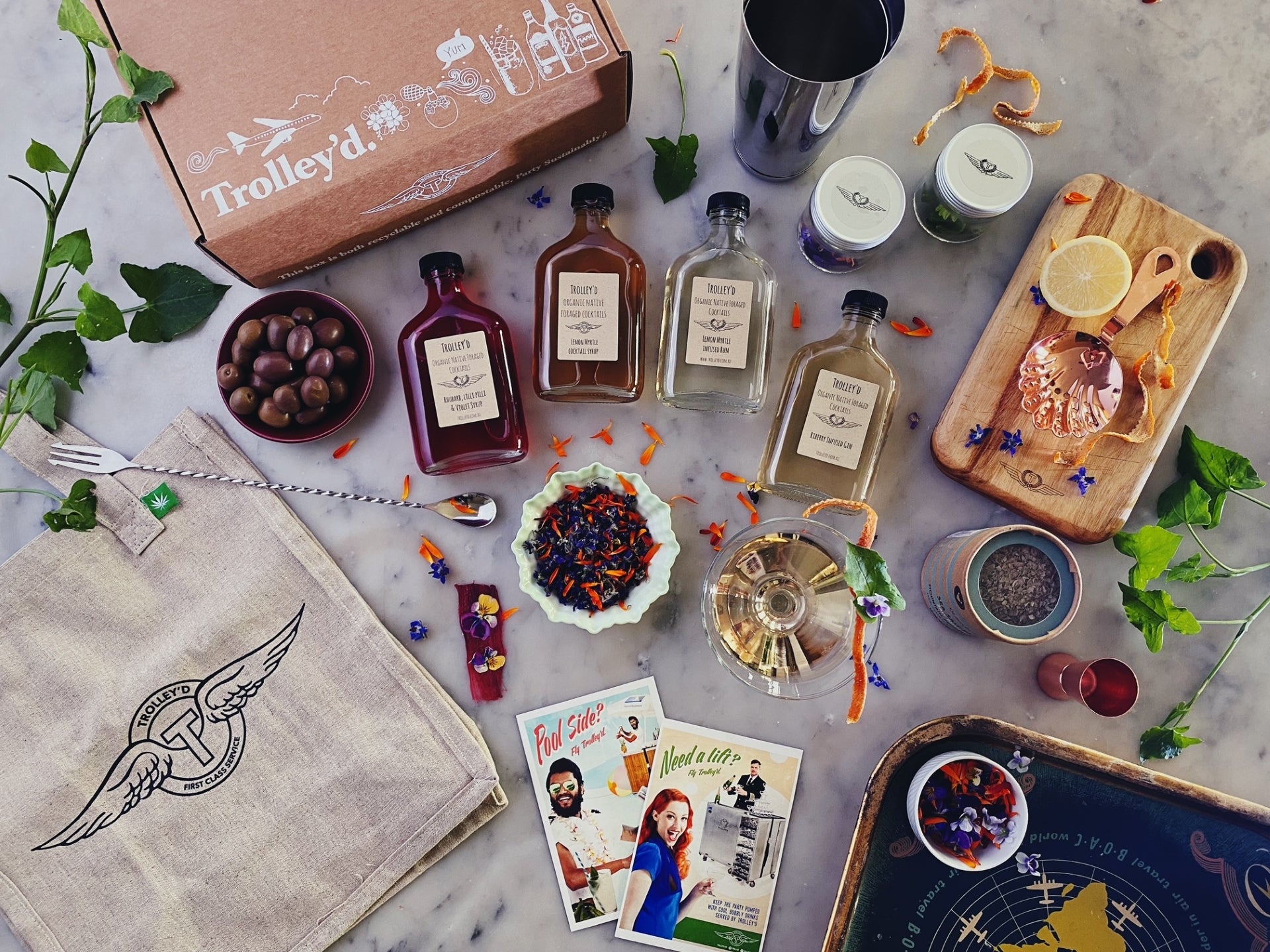 Flat lay of Trolley’d cocktail kit with bottled spirits, syrups, garnish, bar tools and branded packaging for a corporate virtual cocktail class.