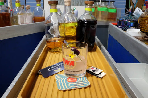 A glass of mulberry-infused clarified milk punch garnished with a flower, displayed with ingredients