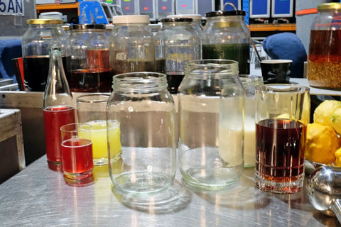 Various jars containing ingredients for making milk punch, including juices, syrups, and milk.