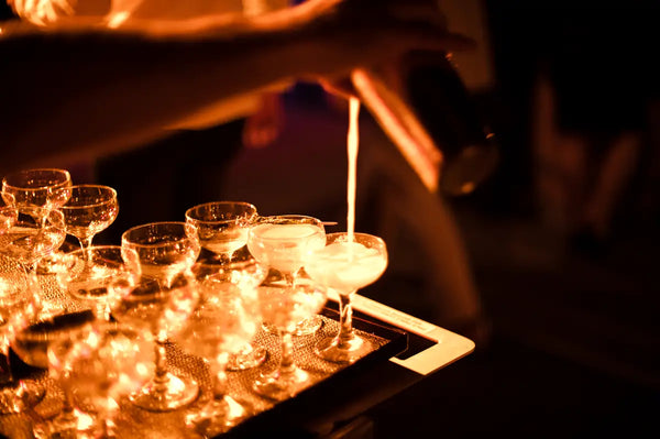 Close-up of a bartender pouring cocktails into glasses at the Australian Bartender Awards 2023, illuminated by warm, ambient lighting.