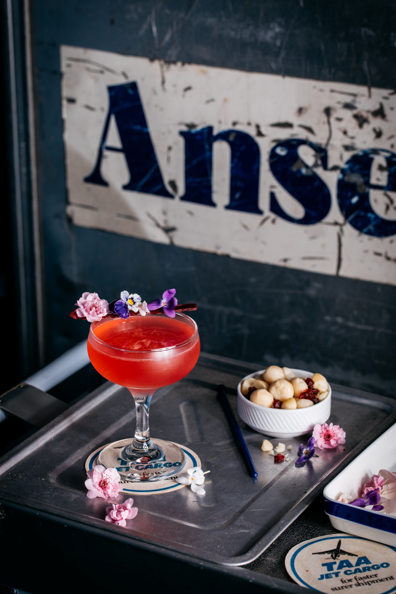 Cocktail with floral garnish on a tray with 'Ansett' sign in the background