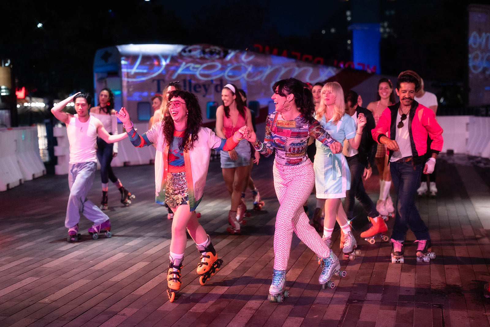 Group of vibrant roller skaters gliding and laughing under neon lights at Neon Dreams, Vivid Sydney 2025, with a retro Trolley’d aircraft bar in the background.