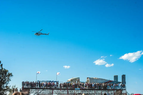 Scaffolding structure at Defqon Festival 2018 with Trolley’d plane bar hoisted on top and a helicopter flying overhead in a clear blue sky.