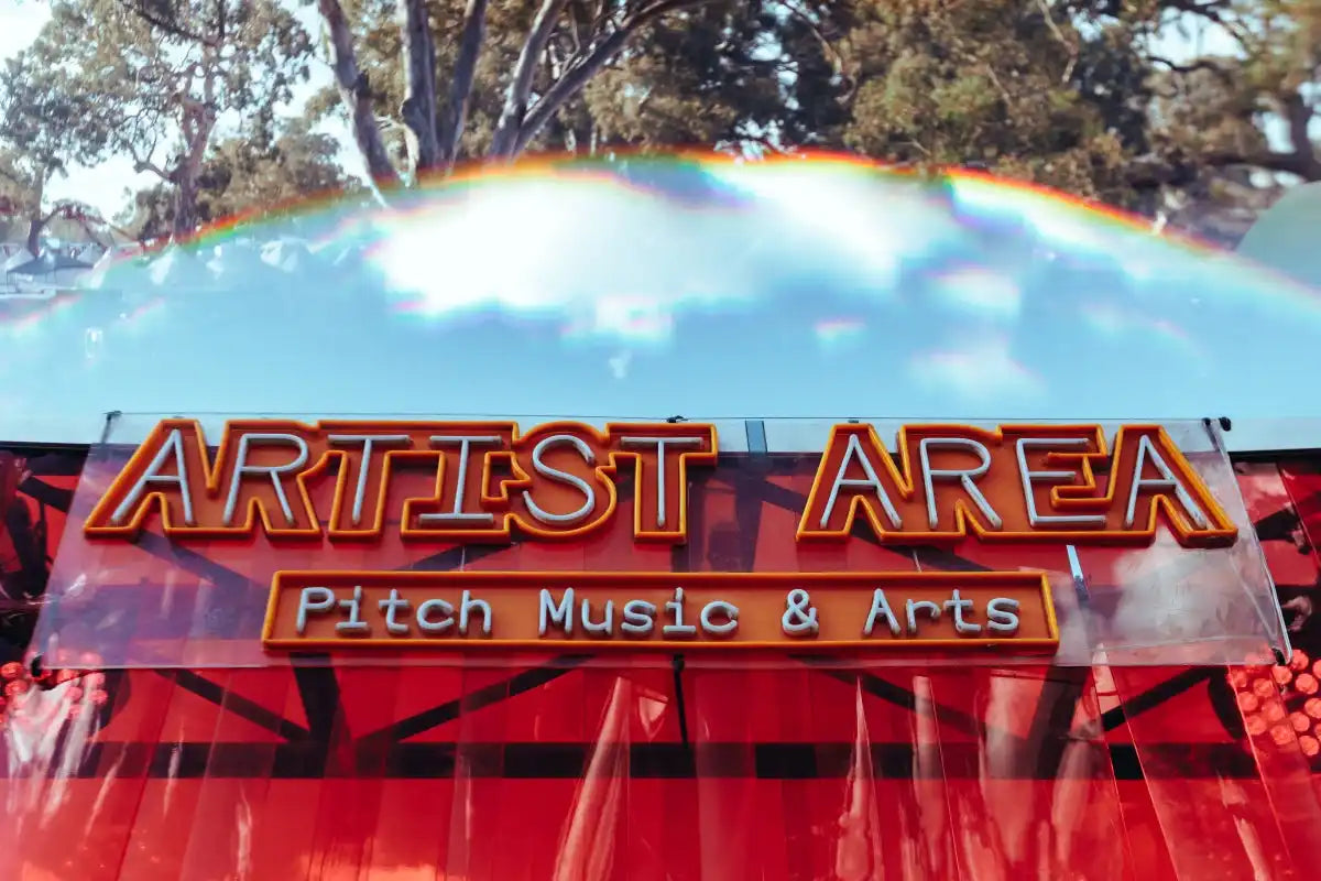 Neon sign reading 'Artist Area' at Pitch Music & Arts Festival with colorful sky background