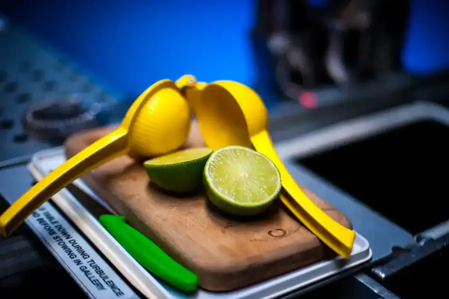 Bright yellow lemon squeezer resting on a wooden cutting board beside halved limes.