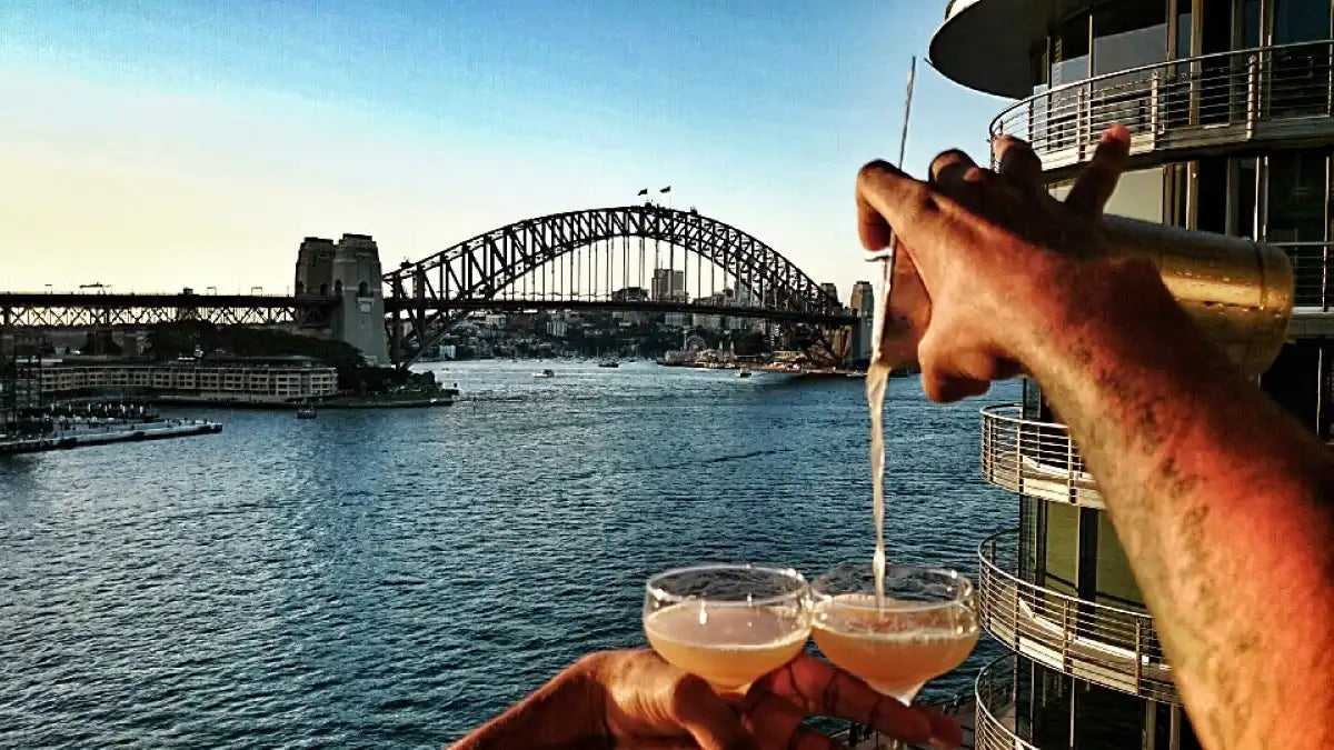 Cocktail glass being filled from a bottle with Sydney Harbour Bridge in the background.