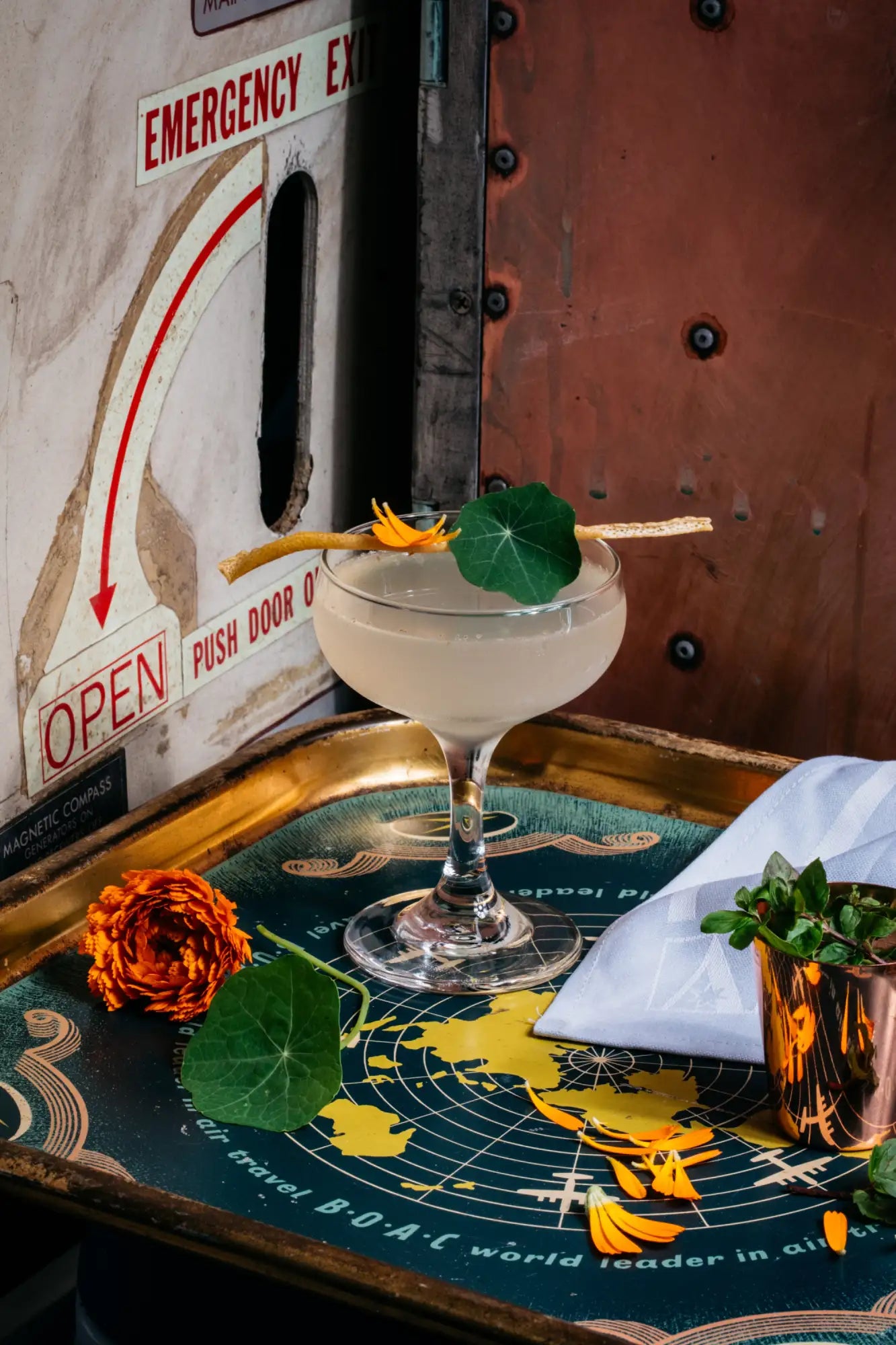 A creamy cocktail in a clear stemmed coupe glass, garnished with a delicate orange flower and green leaf.
