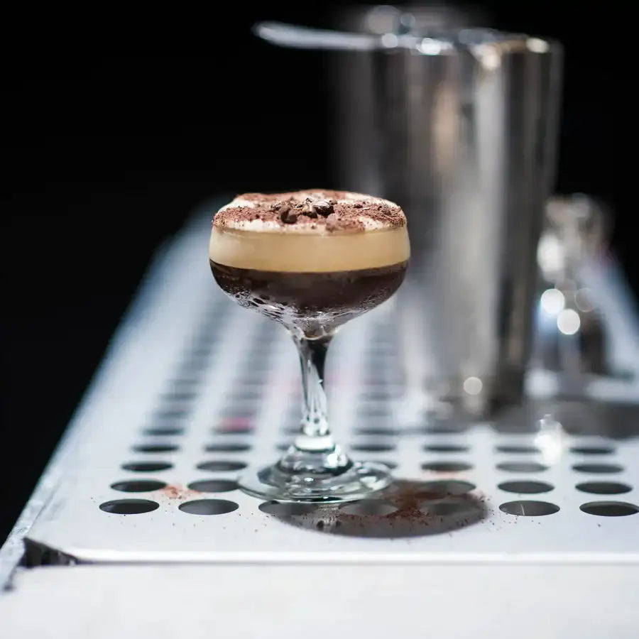 A layered chocolate espresso martini in a clear stemmed coupe glass, topped with cocoa powder and dark chocolate shavings.