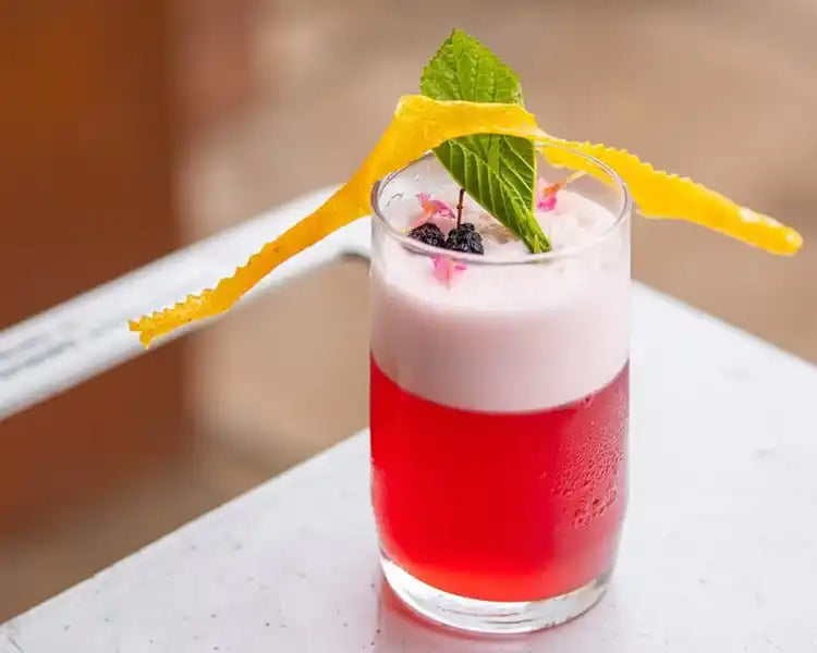 A meticulously crafted cocktail with a vibrant red base and frothy top, adorned with a sprig of mint and a twisted orange peel garnish, ready for participants to enjoy in a Trolley'd mixology class.