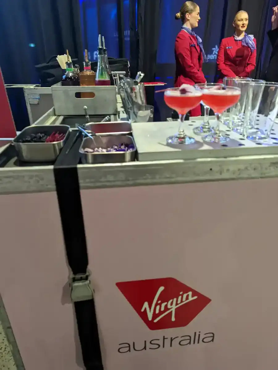 Pink virgin australia branded bar cart with a black strap and stainless steel containers.
