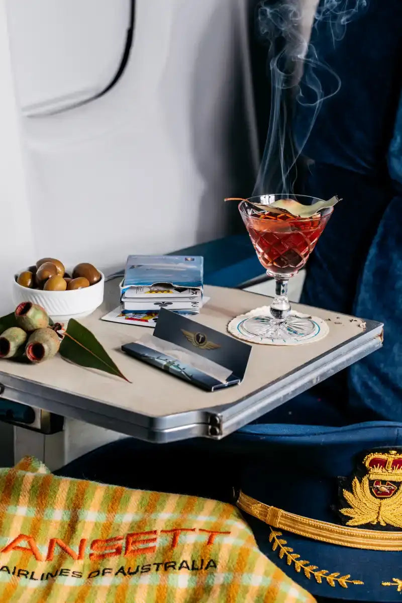 A red cocktail in a faceted martini glass, garnished with an olive and a leaf.