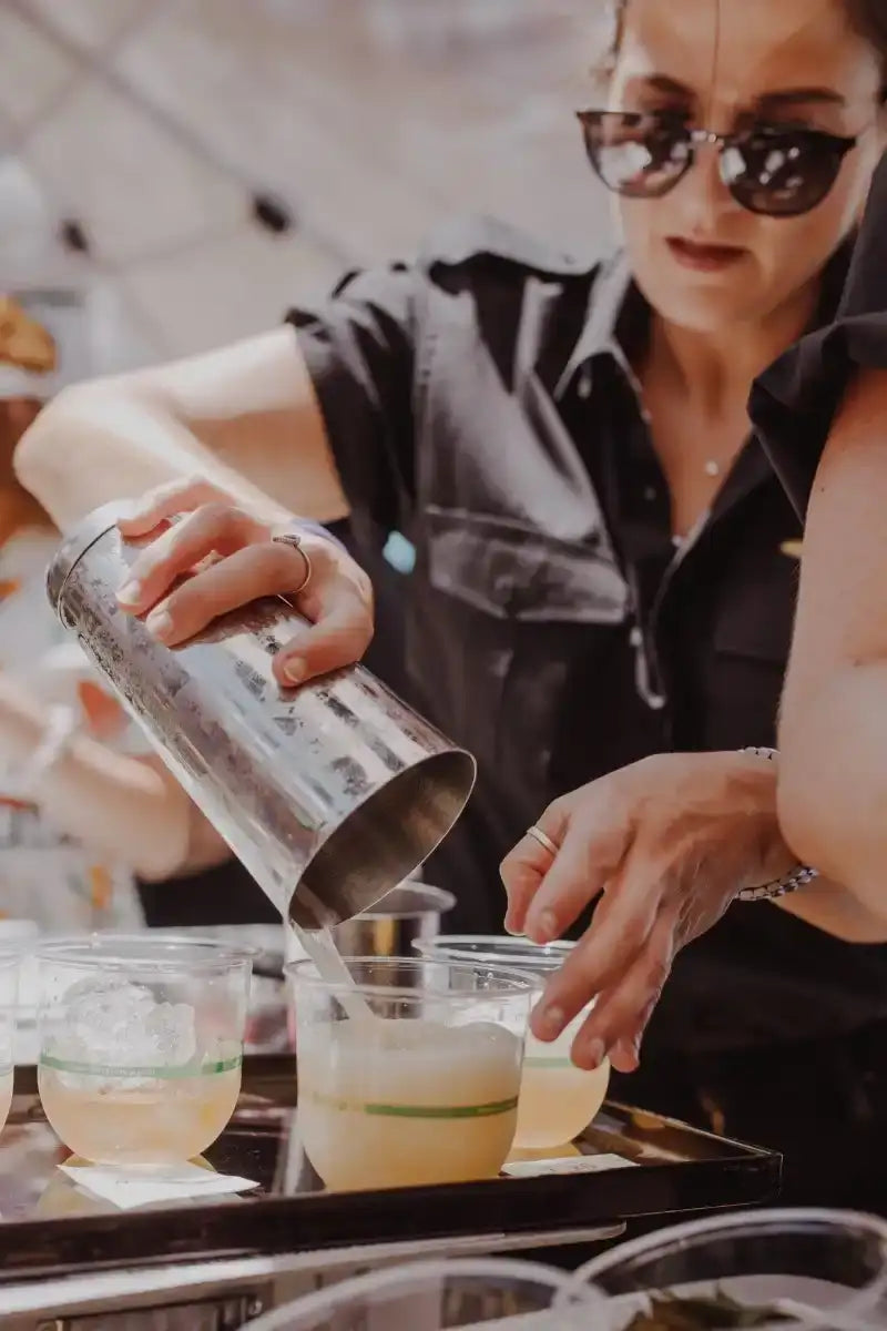 Shiny metallic cocktail shaker being used to pour a drink into glasses.