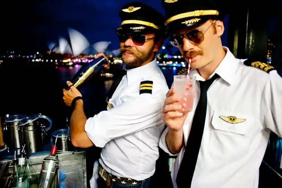 Two men in white pilot uniforms with gold epaulets and black ties, wearing aviator sunglasses and captain hats.