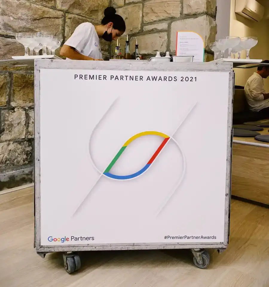 White promotional cart with a colorful google partners logo and ’premier partner awards 2021’’ text, featuring metal wheels.