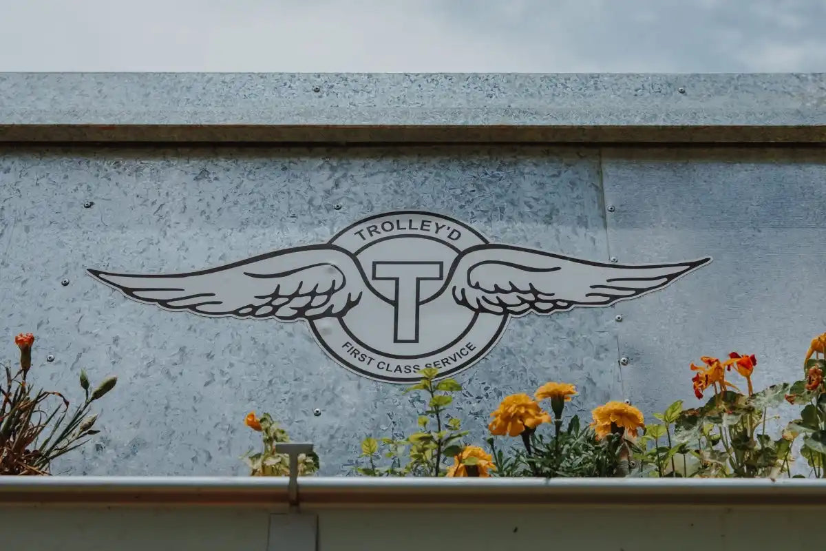 Close-up of Trolley'd's aviation-themed bar logo on a galvanized metal surface, showcasing their commitment to first-class service and unique bar experience.