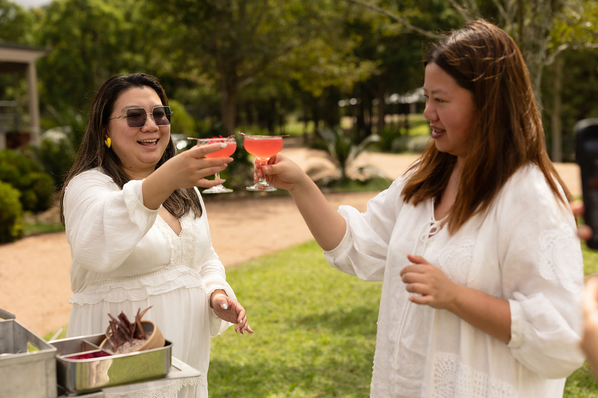 Two guests raise red botanical cocktails beside the Trolley’d bar at Lake David